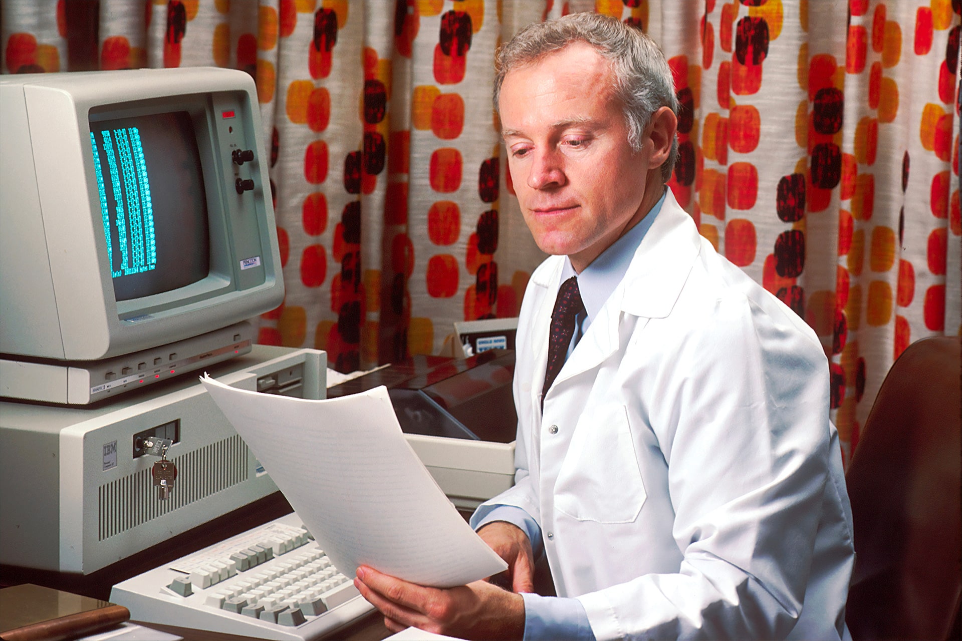 Doctor reviewing documents with vintage computer.