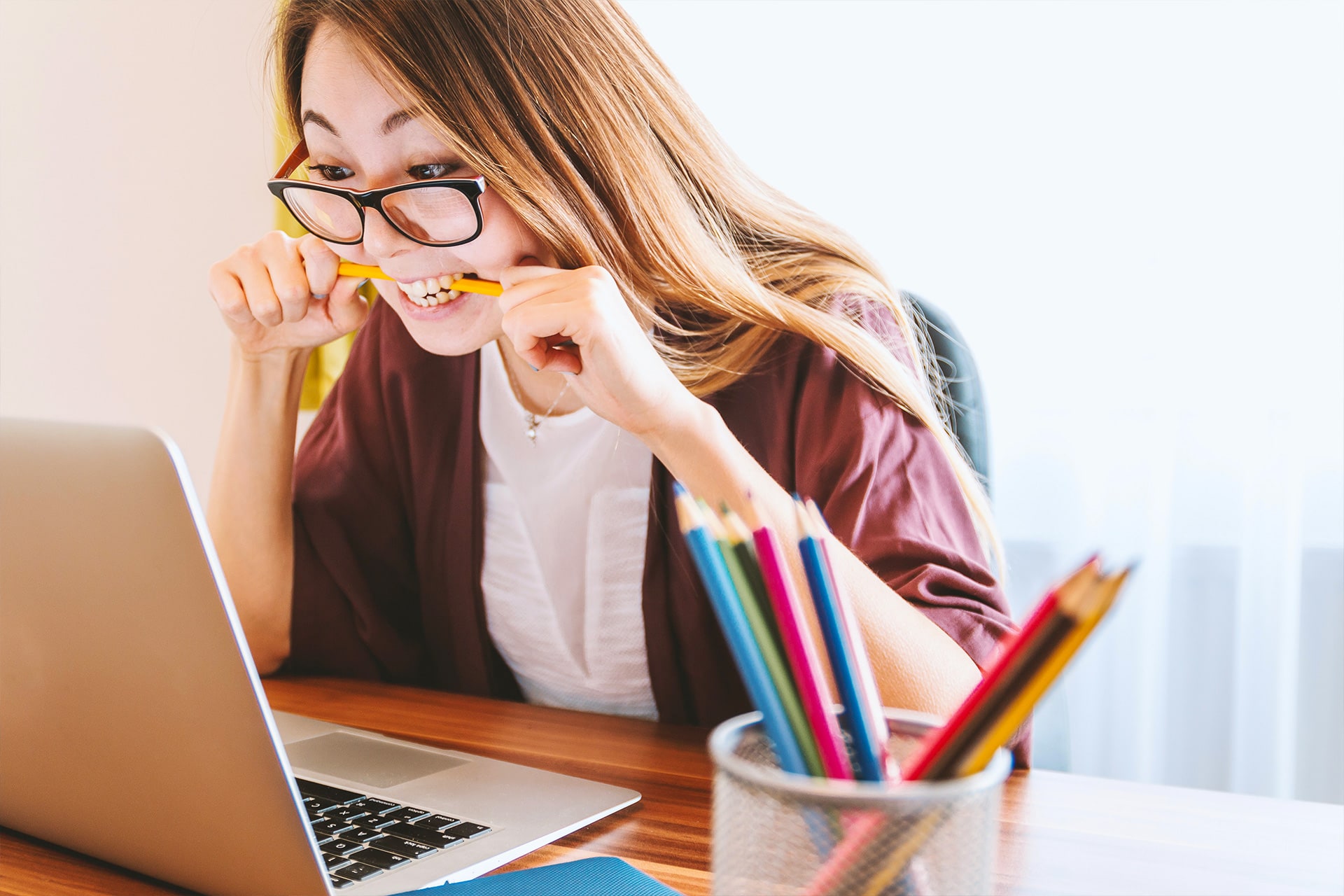 Stressed woman biting pencil at laptop