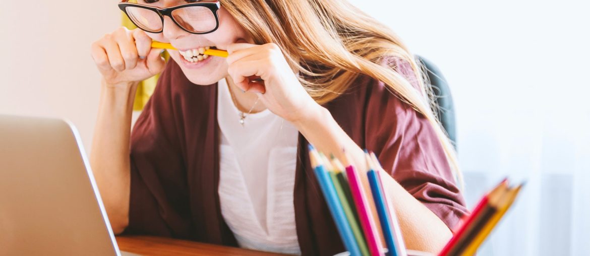 Stressed woman biting pencil at laptop