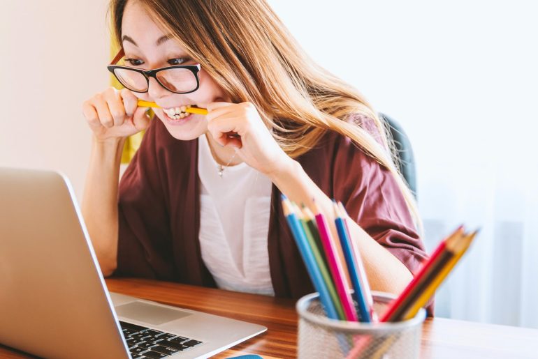 Stressed woman biting pencil at laptop