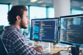 Person coding at computer desk in office.