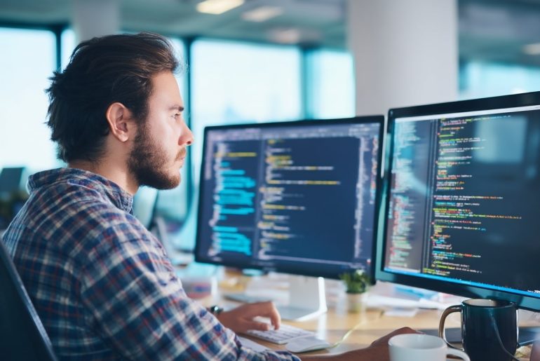 Programmatore al lavoro su computer multi-schermo