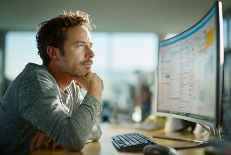 Homem olha para uma tela de computador, pensando intensamente.