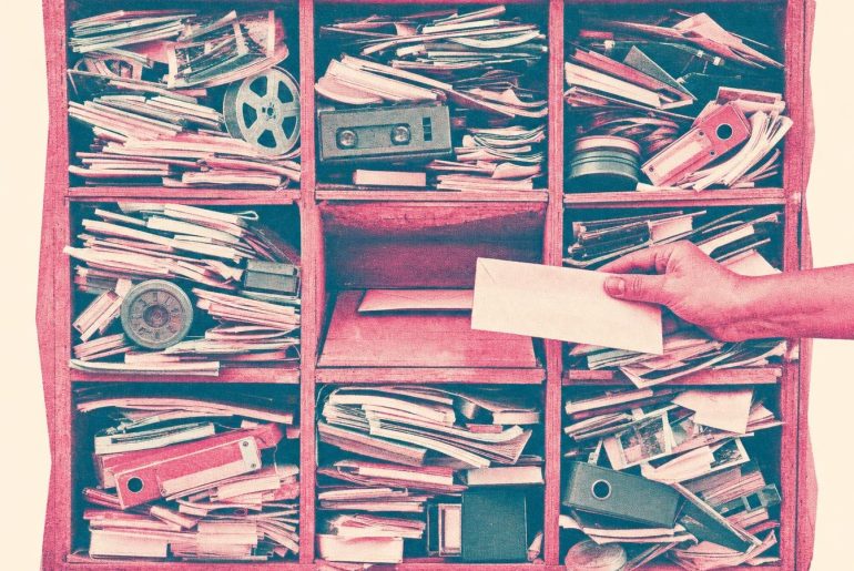 Escaninho com oito compartimentos a transbordar de fotografias, bobinas e dossiês e um compartimento central quase vazio onde uma mão introduz uma carta